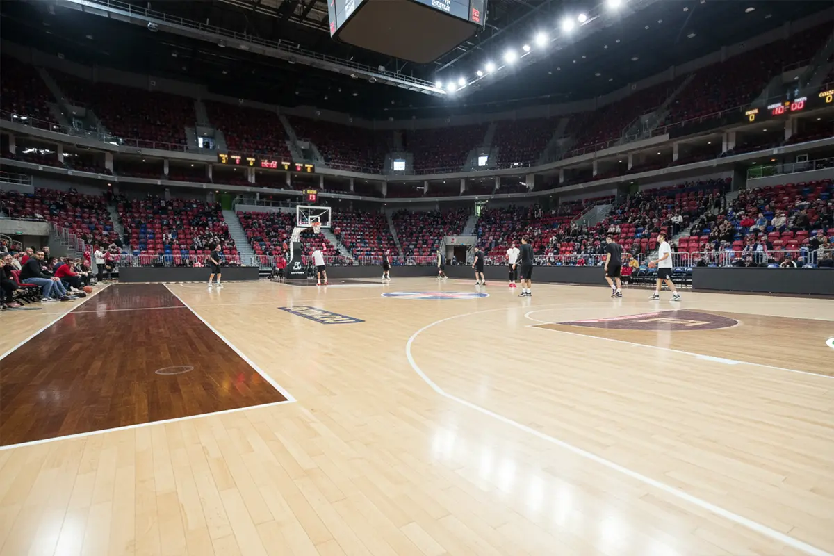 Pista de baloncesto profesional europea con parqué brillante y marcadores electrónicos visibles durante un partido de Euroliga